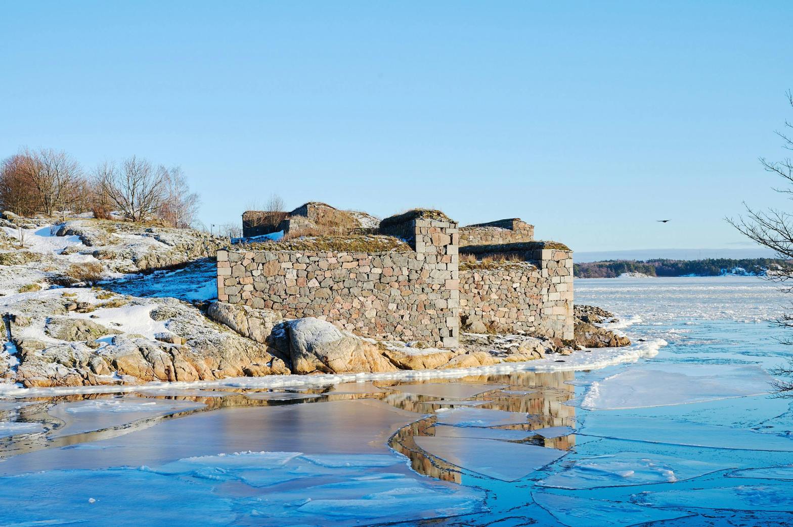 Suomenlinnan linnoituksen kiviset muurit talvisessa saaristomaisemassa Helsingissä, jäätyneen meren rannalla.